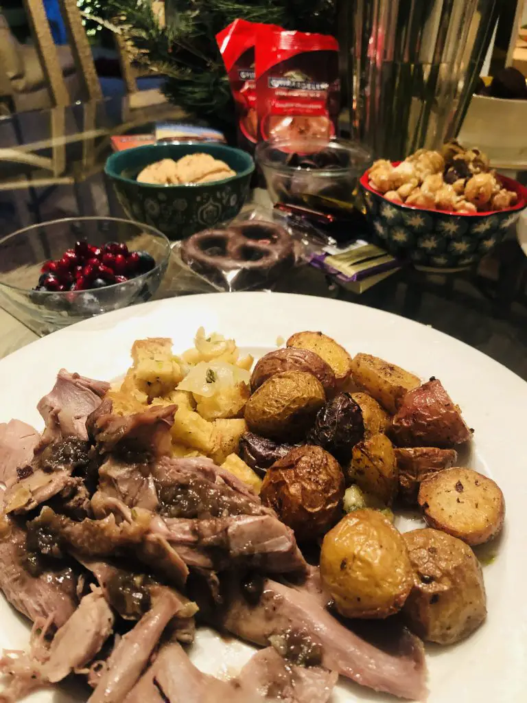 goose fat roasted potatoes along with goose meat and sage and onion stuffing on a white plate with various desserts in the background such as chocolate pretzels, caramel corn, cookies, and pomegranate seeds