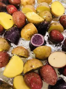 Colorful pieces of new potatoes in goose fat with salt and pepper sprinkled over them on a sheet of aluminum foil