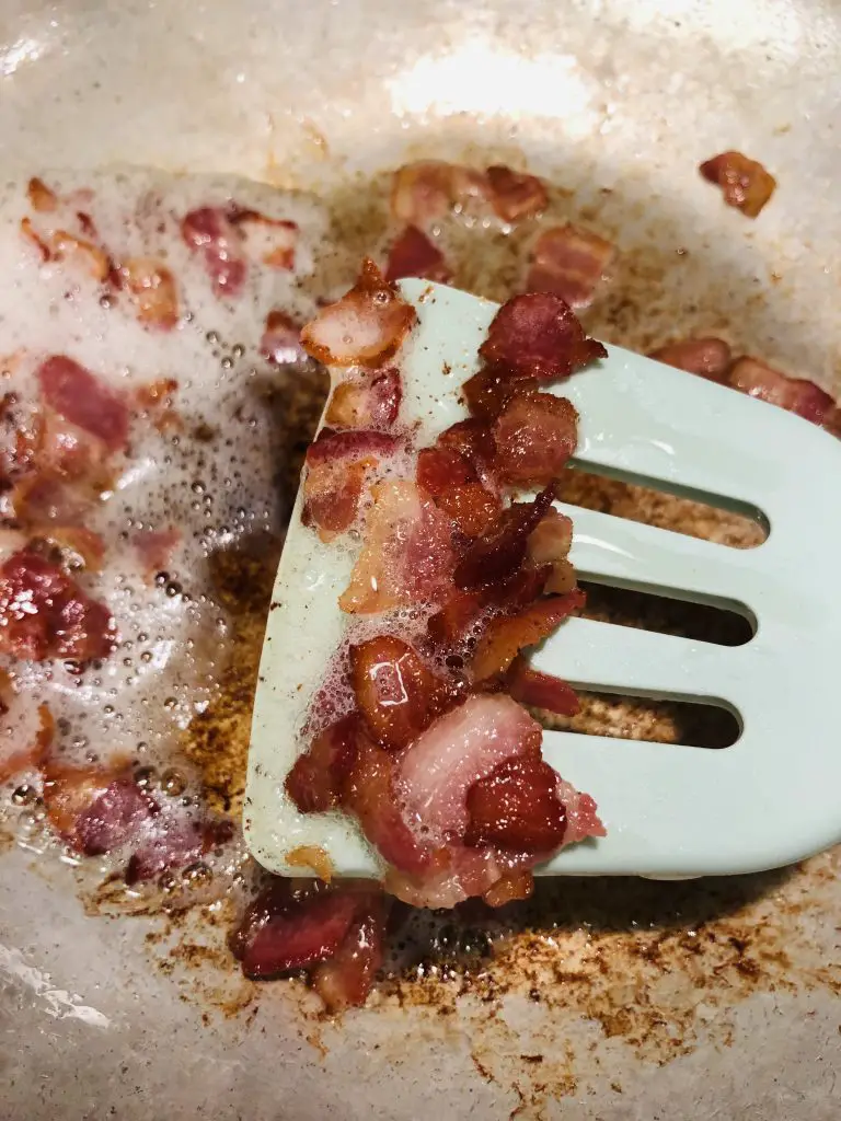 crispy small pieces of bacon on a blue slotted turner in a frying pan