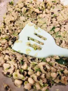 black eyed peas, minced onion, garlic, and jalapeno peppers in a frying pan with a blue silicone utensil mashing the beans
