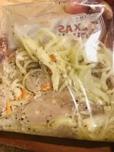 Chicken, onions, garlic, ginger, and scotch bonnet peppers in a marinade in a plastic bag