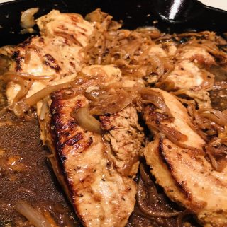 Chicken yassa consisting of chicken breasts and caramelized onions in a cast iron skillet