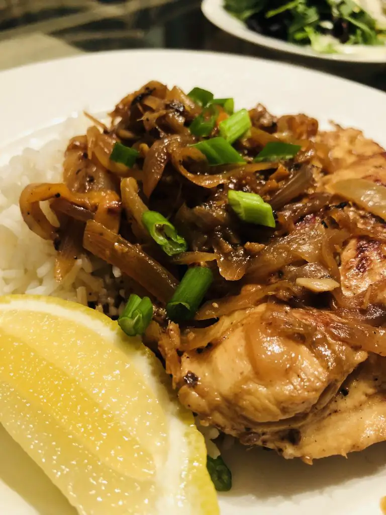 Chicken yassa served with rice with a lemon wedge and garnished with green onions on a white plate