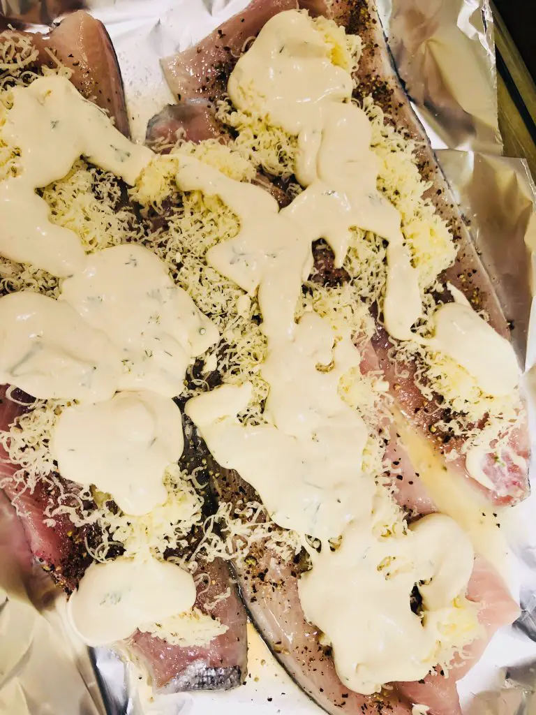 fish fillets covered with cheese and a cream sauce in a baking tray lined with Aluminum foil