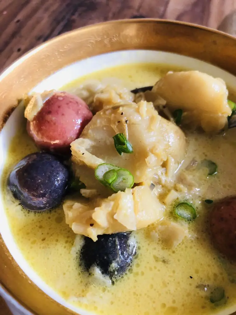 Icelandic Fish Stew including cod, potatoes and chopped green onions in a gold rimmed bowl
