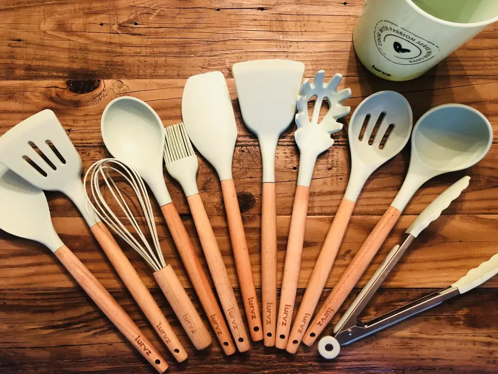 Entire set of Lurvz silicone utensils laid out on a wooden board with their storage barrel in the background
