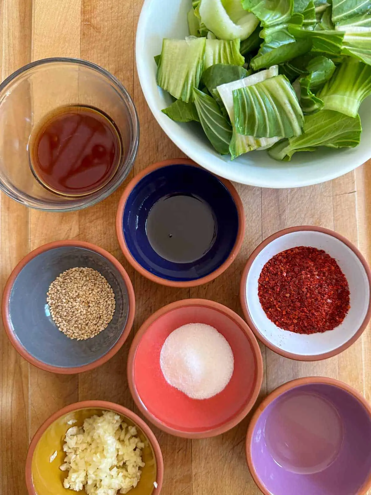 Bowls containing cut up baby bok choy, fish sauce, rice vinegar, sesame oil, sesame seeds, sugar, Korean red pepper flakes, and minced garlic.