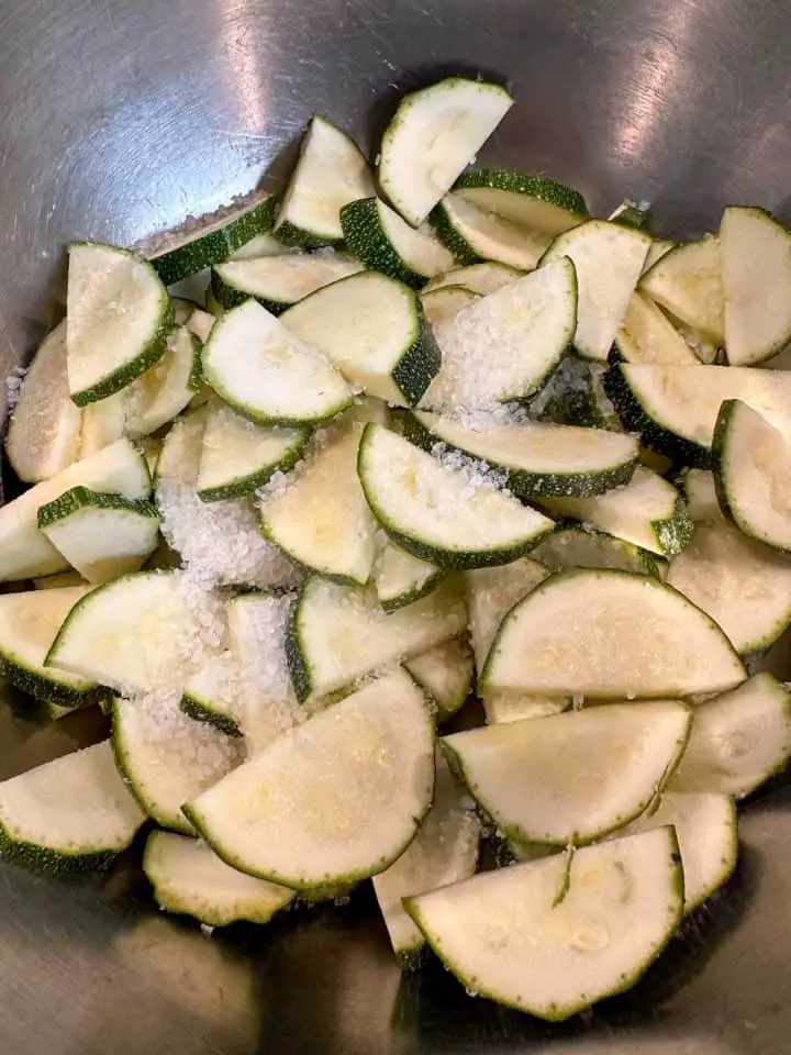 Slices of zucchini in a silver bowl that have been sprinkled with salt.