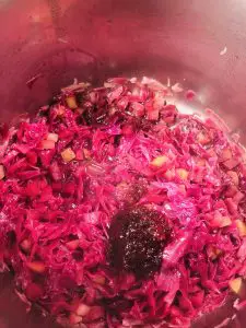 sliced red cabbage and apples in a pot with red currant jam