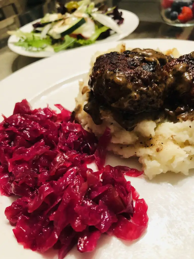 Danish red cabbage served with mashed potatoes and meatballs, with salad and fruit in the background