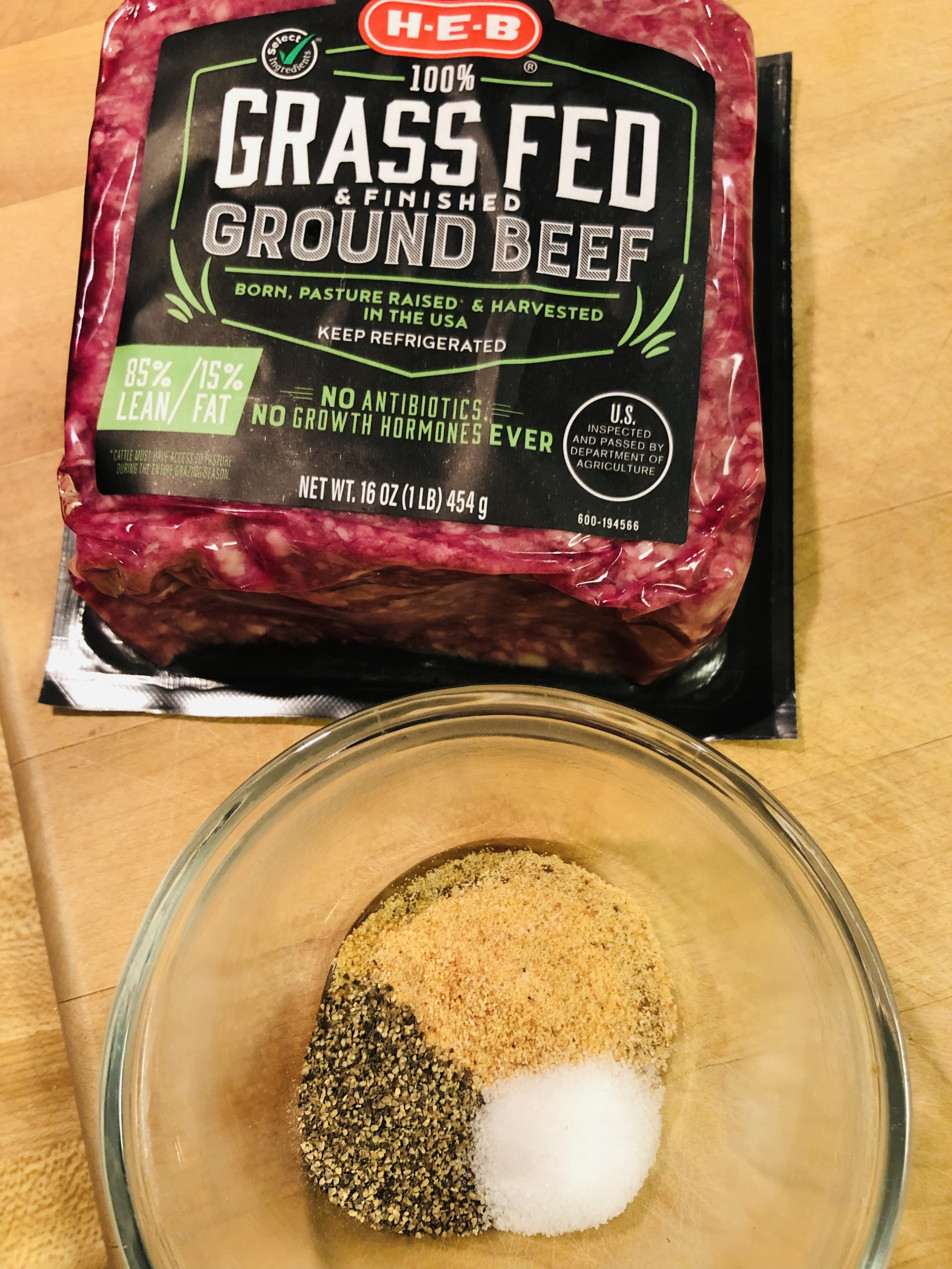 a package of ground beef and salt, pepper, and garlic powder in a glass bowl