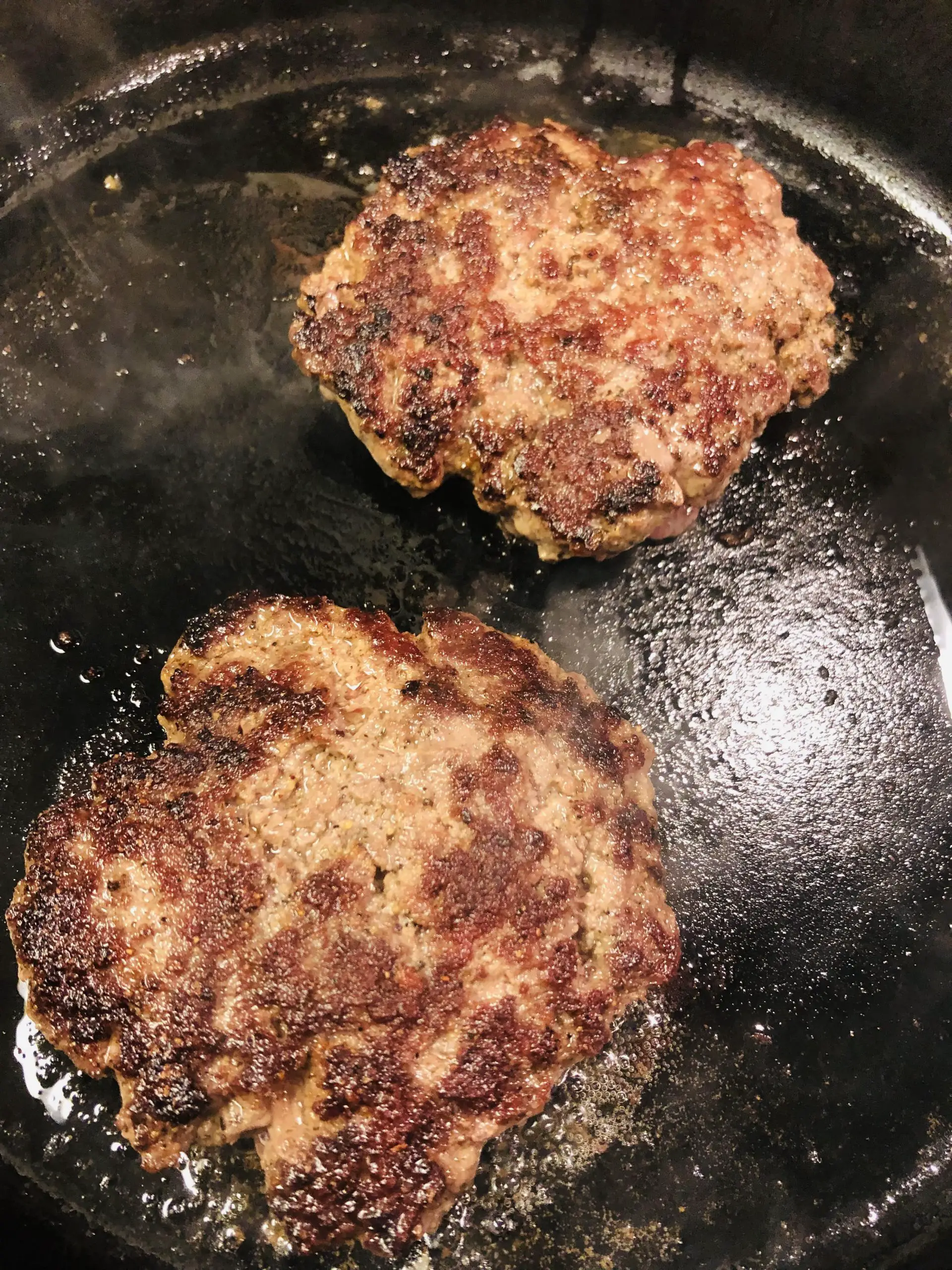 cooked hamburger patties in a cast iron skillet