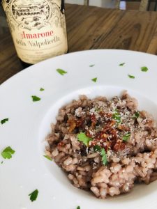 Amarone Red Wine Risotto in a white dish with parsley scattered and a bottle of Amarone next to it