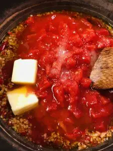 chopped tomatoes and butter in a saucepan with garlic, chilies, and olive oil and a wooden spoon on the side