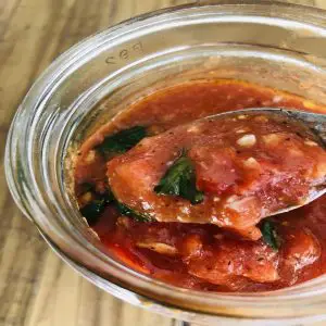 Tomato sauce in a glass jar with some of the sauce in a spoon
