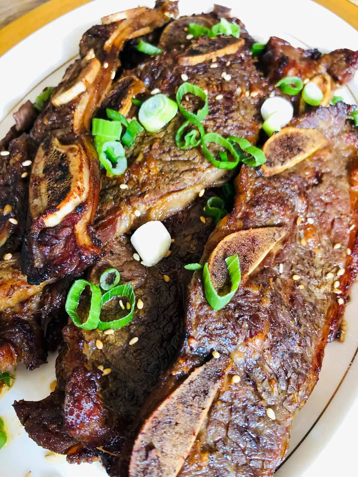 Korean short ribs (kalbi) on a gold rimmed plate garnished with green onions.