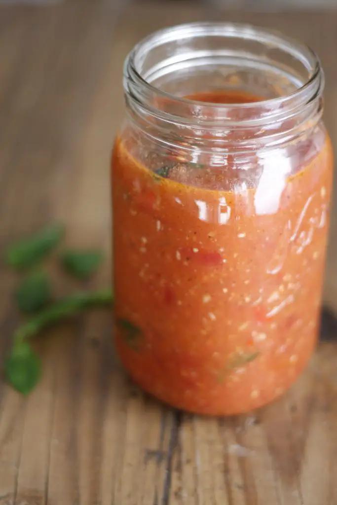 tomato sauce in a glass jar with some basil scattered on the side