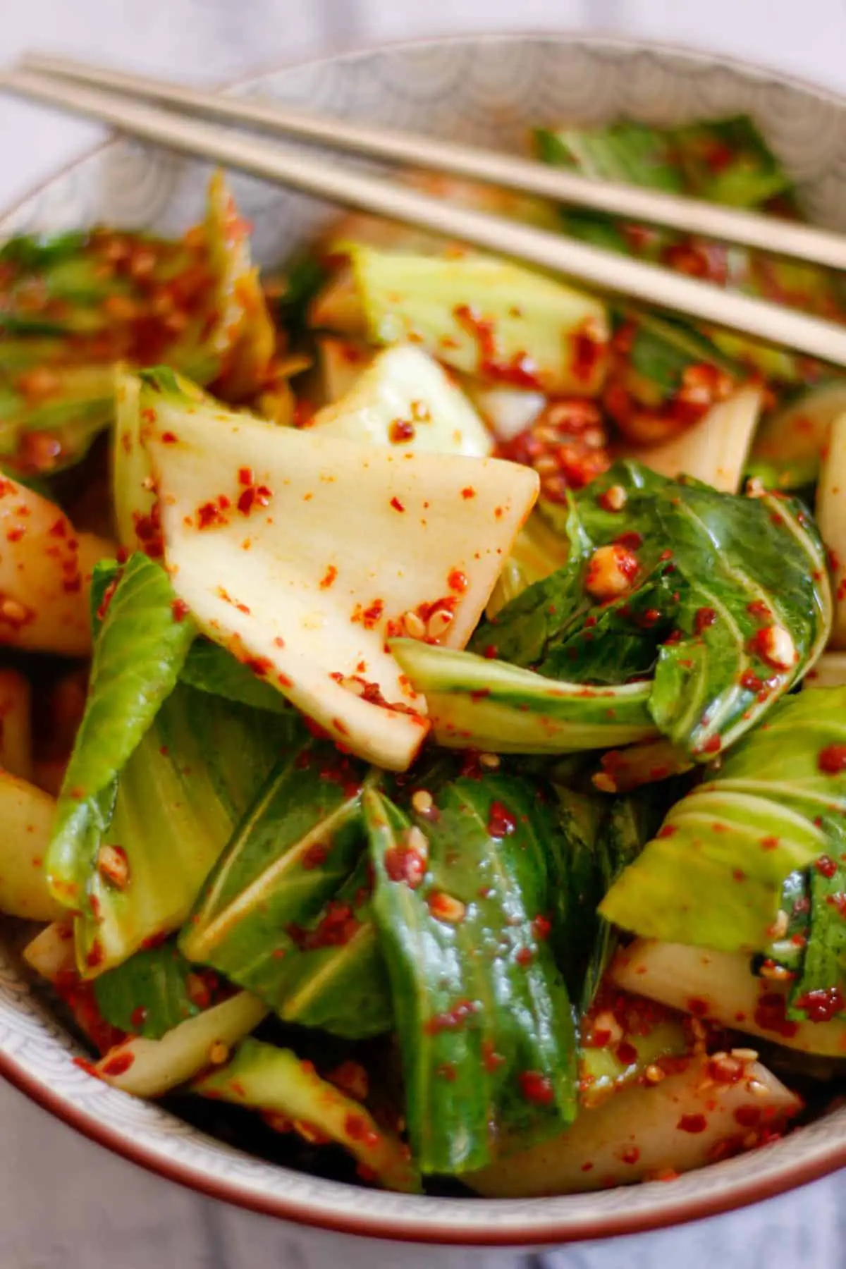Bok choy kimchi in a bowl with a set of silver chopsticks resting on the side of the bowl.