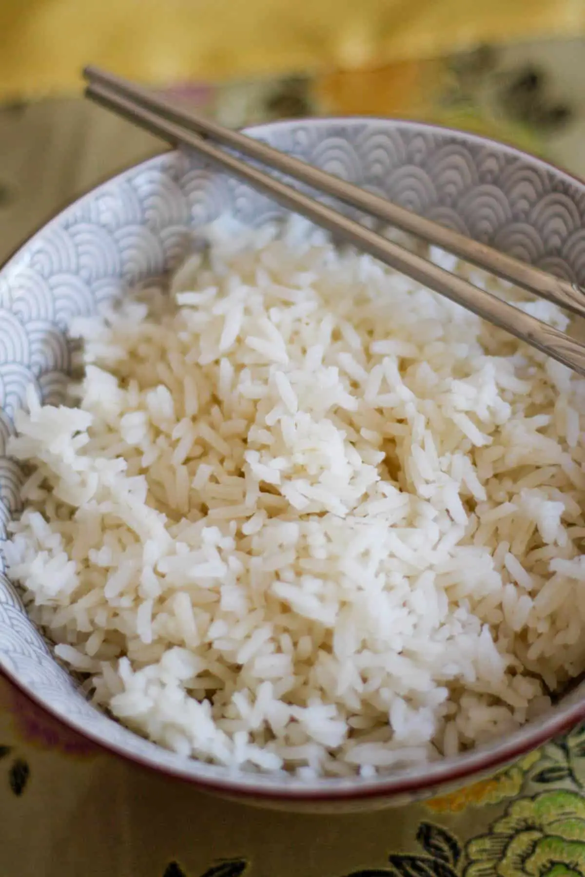 A patterned bowl containing steamed rice. There is a pair of silver chopsticks resting across the bowl.