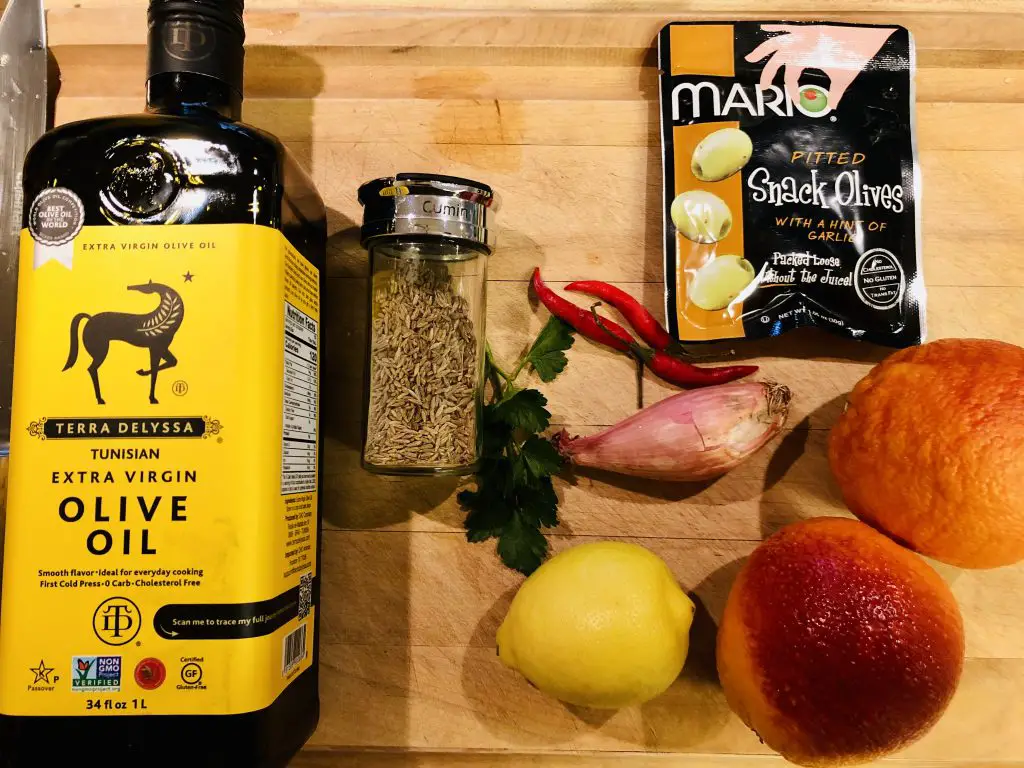 Olive oil, cumin, parsley, red chilies, lemon, blood oranges, and olives on a wooden board