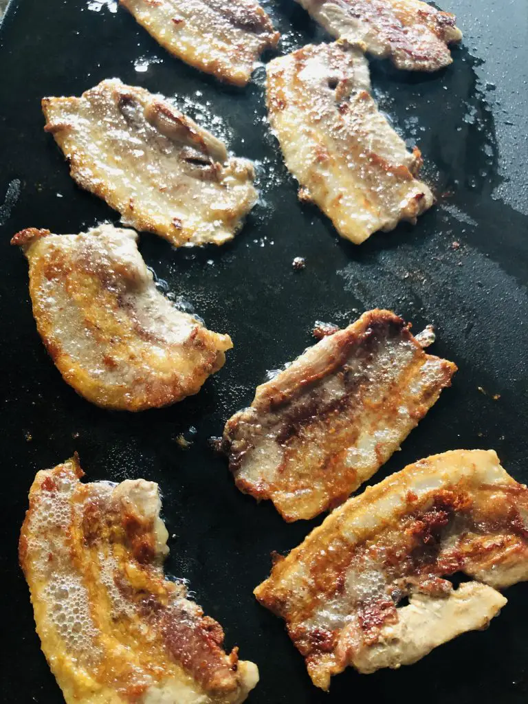 pieces of pork belly frying on a griddle