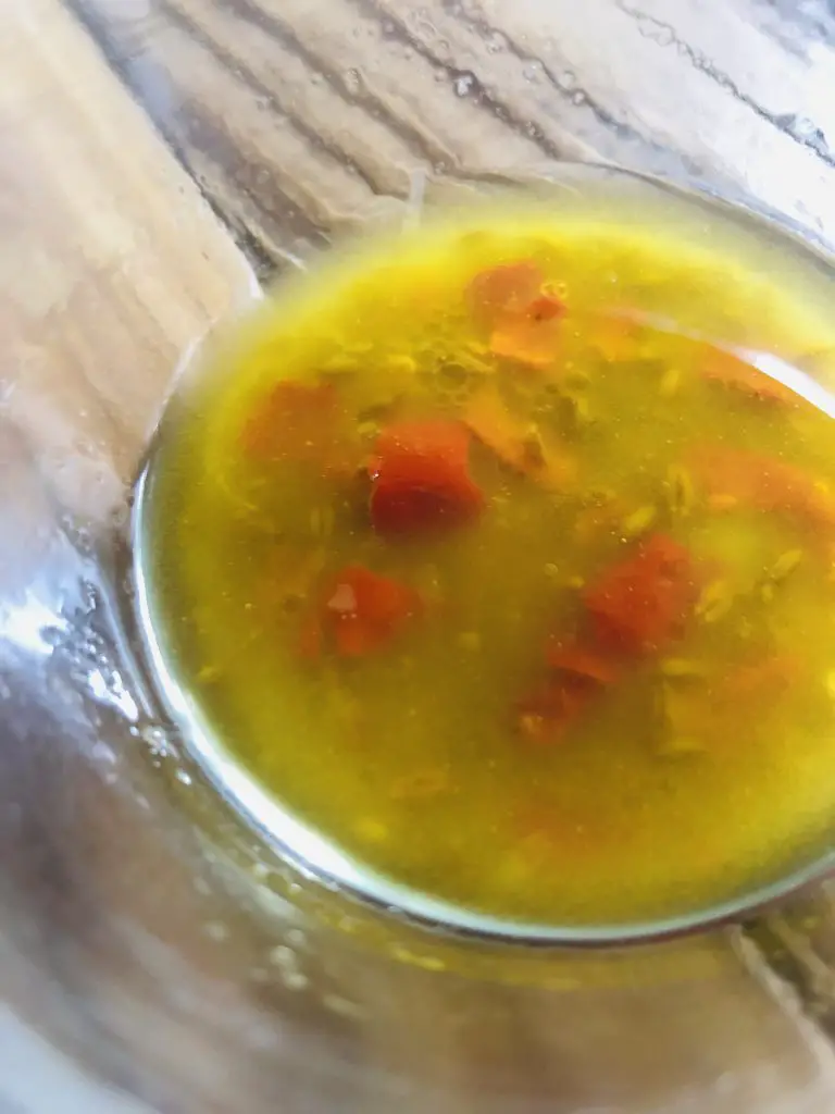 olive oil dressing including chilies and cumin seeds in a glass bowl