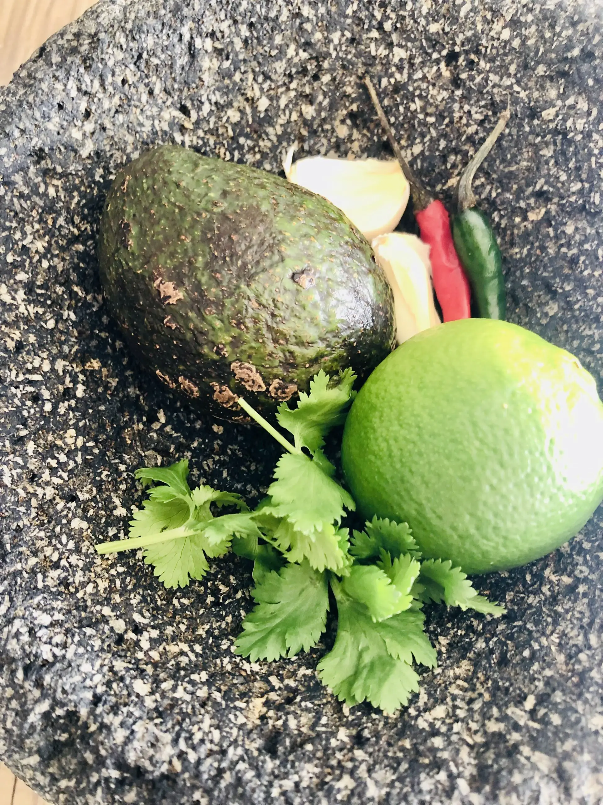 Molcajete containing an avocado, cilantro, lime, garlic, and Thai chilies