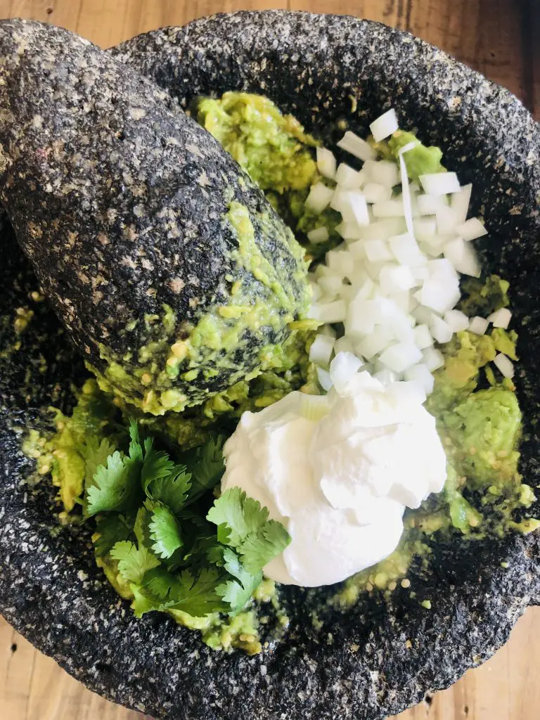 guacamole with minced onion, cilantro, and sour cream in a molcajete with a pestle