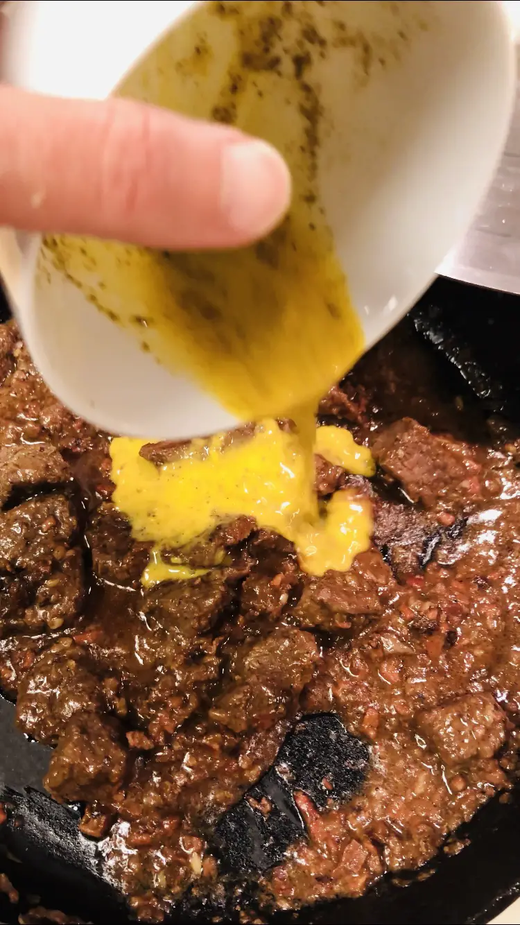 Egg and lemon sauce from a white bowl being added to braised lamb