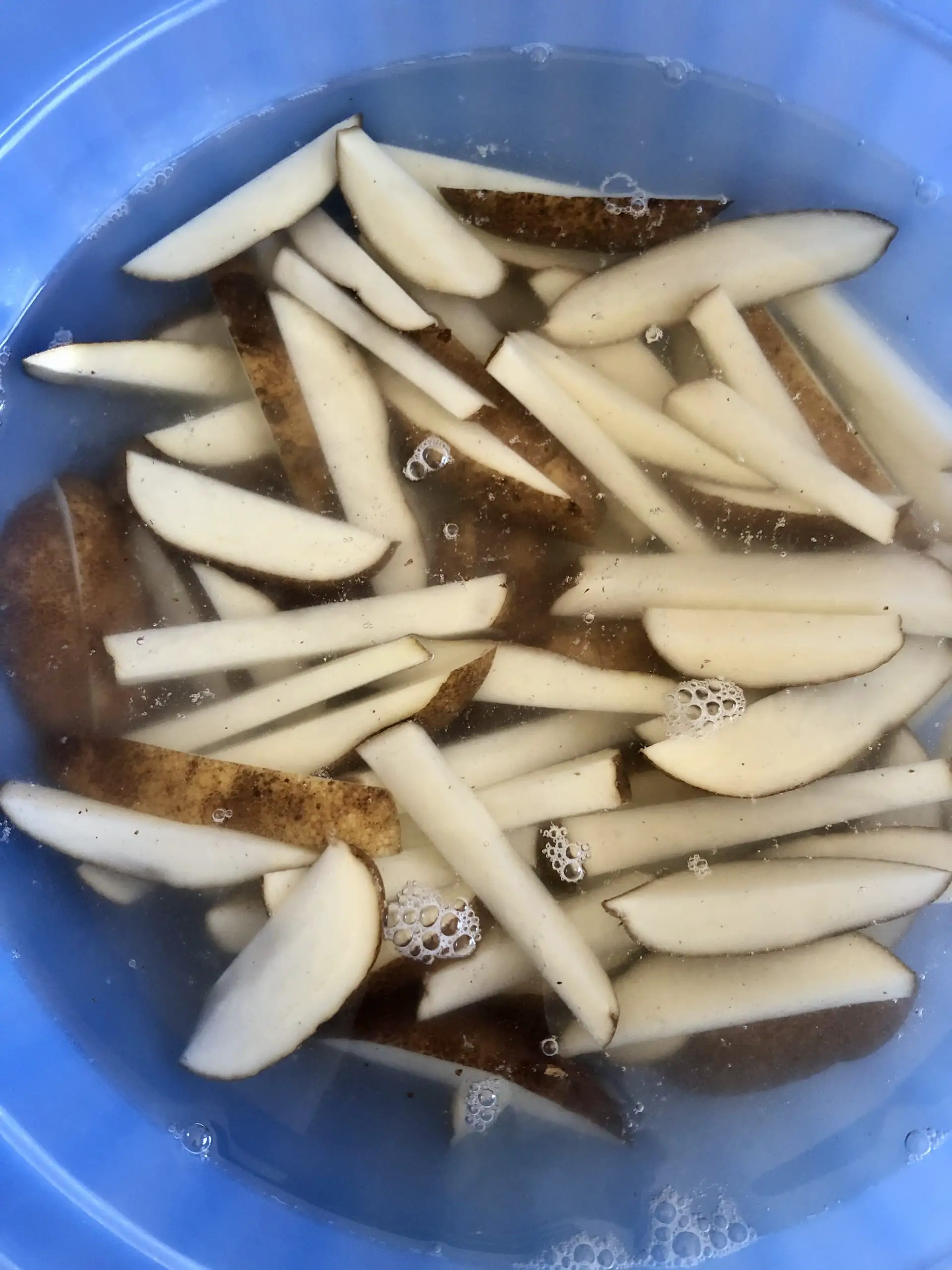 strips of russet potato soaking in water in a blue bowl