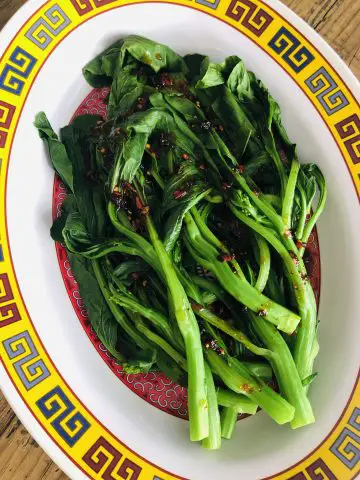 Yu Choy drizzled with spicy sauce on a colorful platter