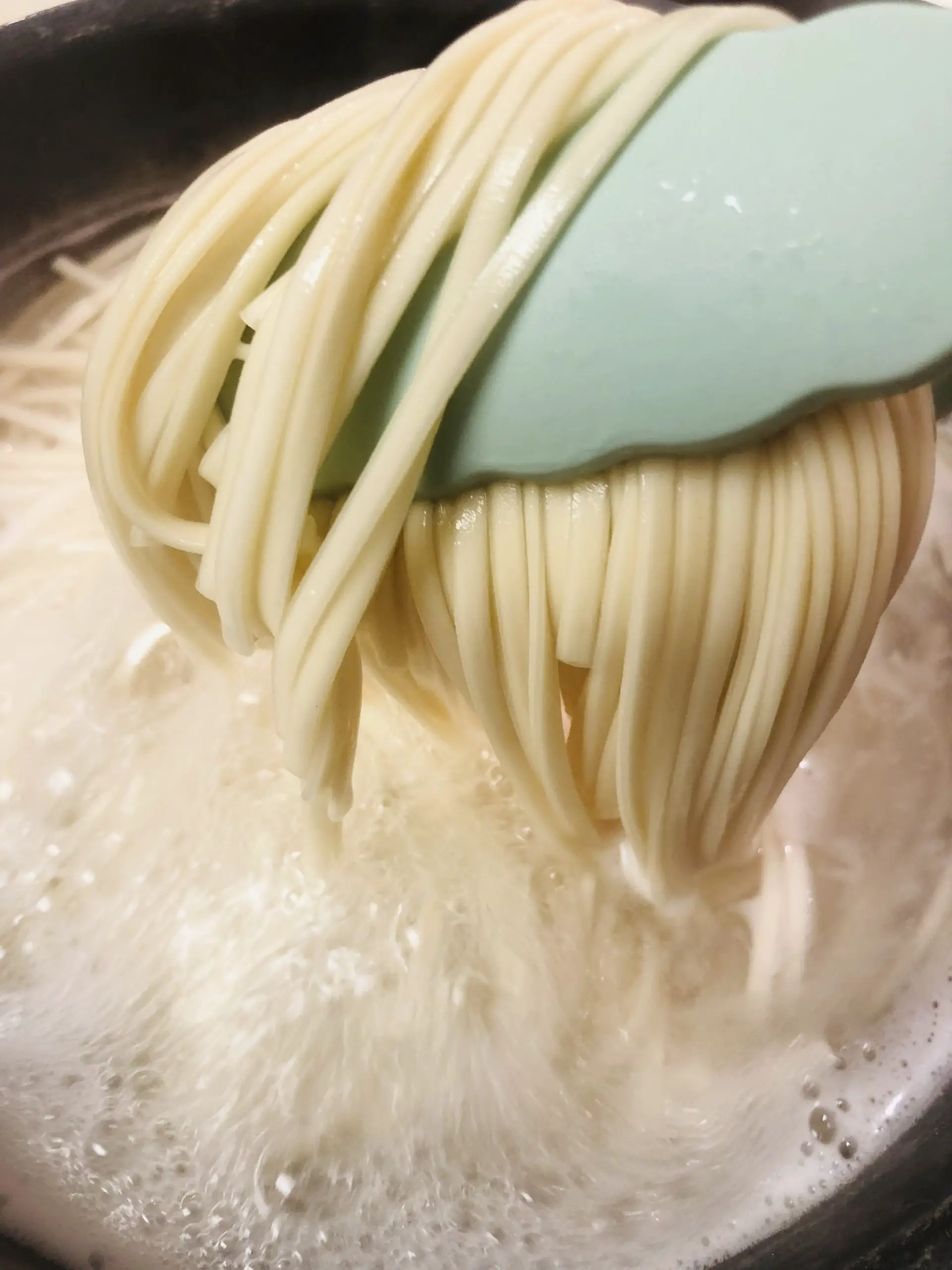 noodles held by tongs over boiling water