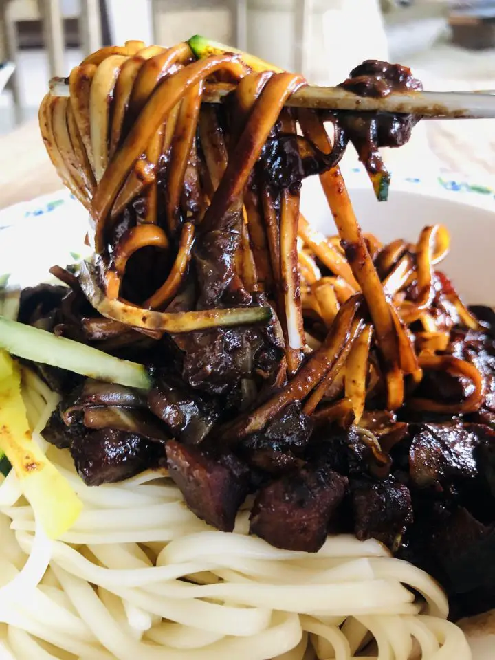 Jajangmyeon noodles and black bean sauce with cucumber matchsticks and chopsticks holding up the noodles