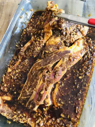 Korean Short Ribs in a marinade in a glass dish with tongs before baking