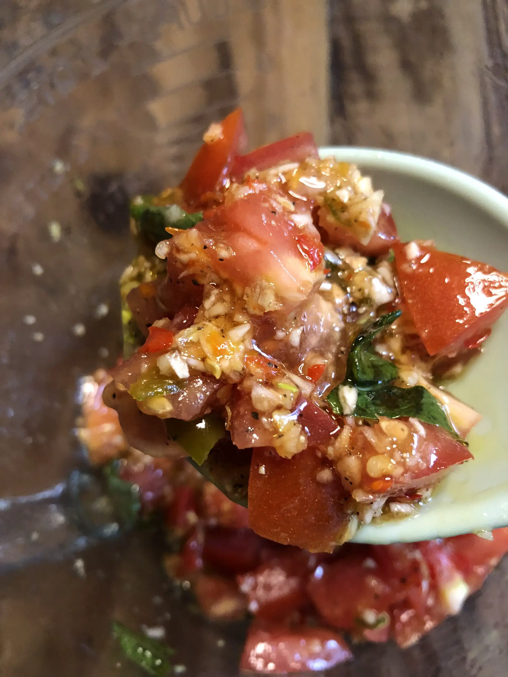 a blue spoon holding a sauce consisting of olive oil, garlic, diced tomatoes, chilies, and basil leaves