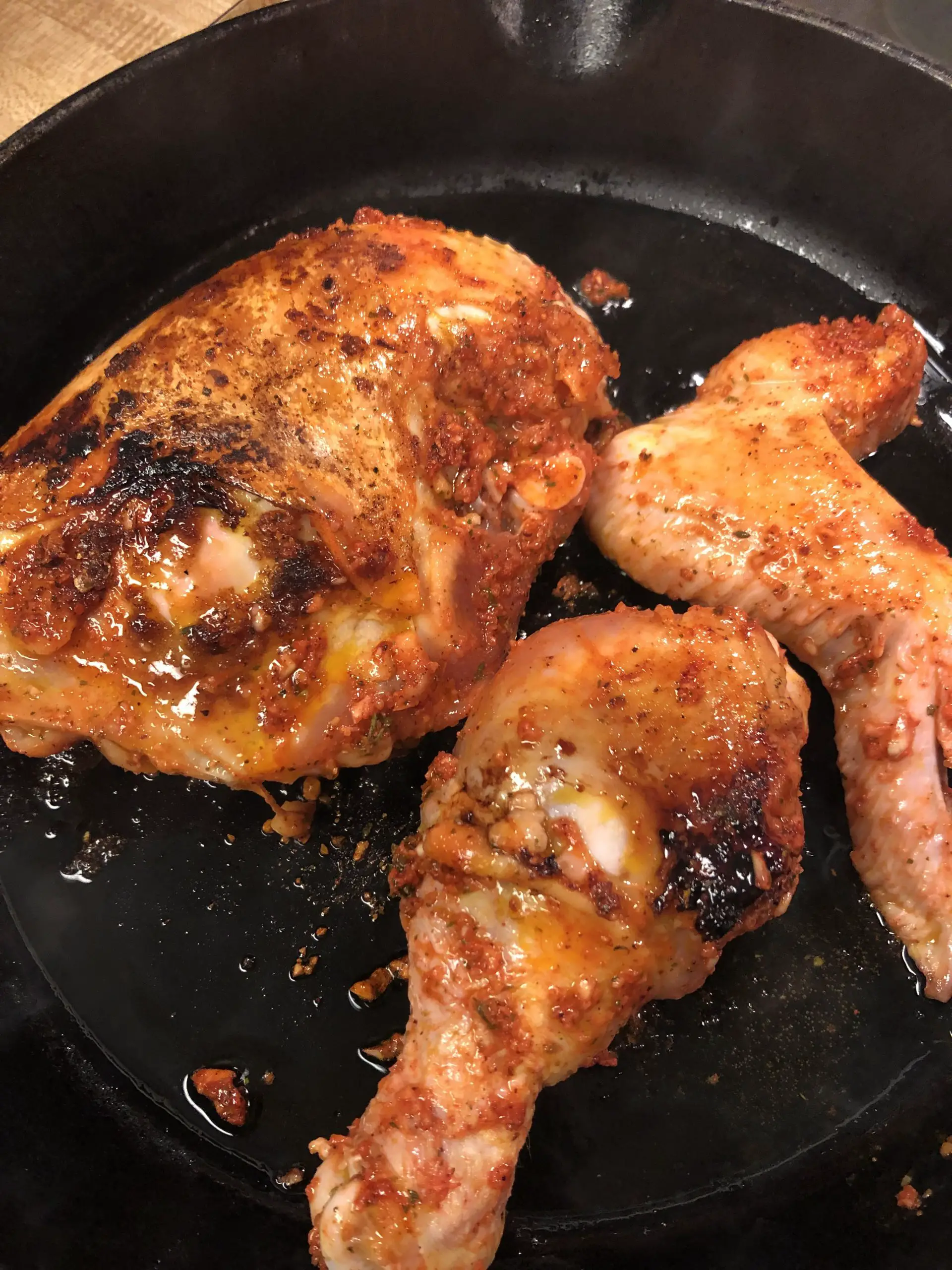 Pieces of chicken frying in a cast iron pan