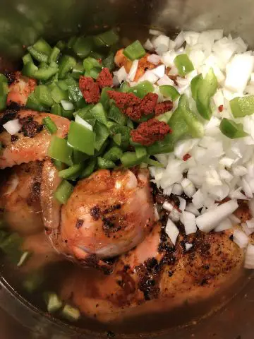 Chicken pieces, diced onion and green bell pepper, achiote rojo paste in chicken broth in a large pot
