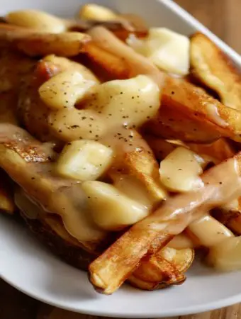 Poutine consisting of fries covered with cheese curds and gravy in a white dish
