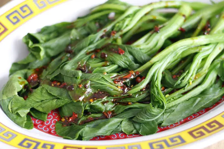 Yu Choy on a plate drizzled with a spicy sauce