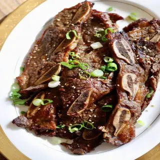 Korean Short Ribs on a gold rimmed plate garnished with green onions and sesame seeds