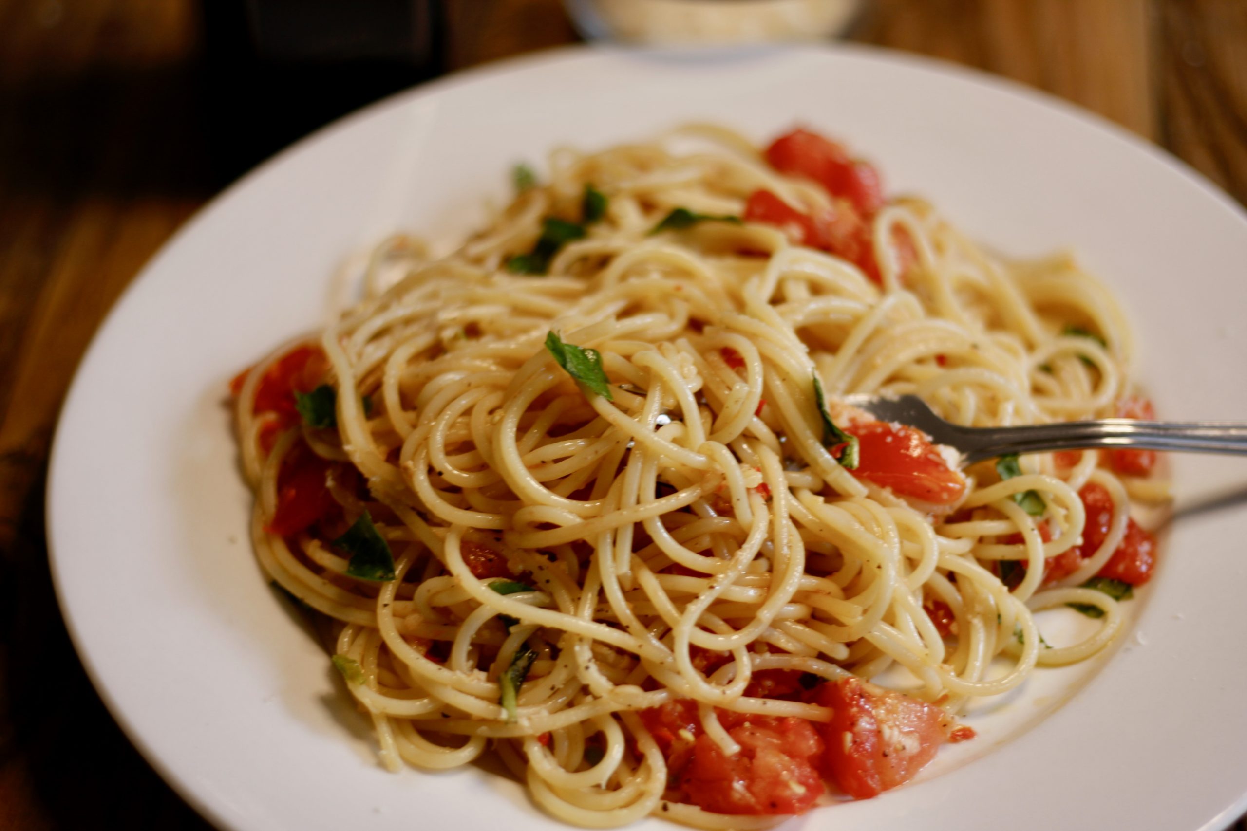 spaghetti with tomatoes and basil leaves topped with grated Parmigiano Reggiano on a white plate