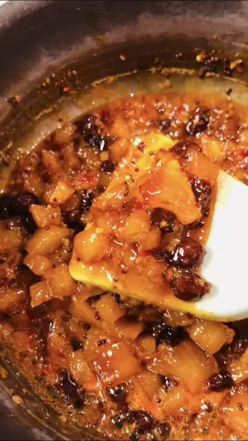 Mango chutney in a saucepan and some of it on a utensil.