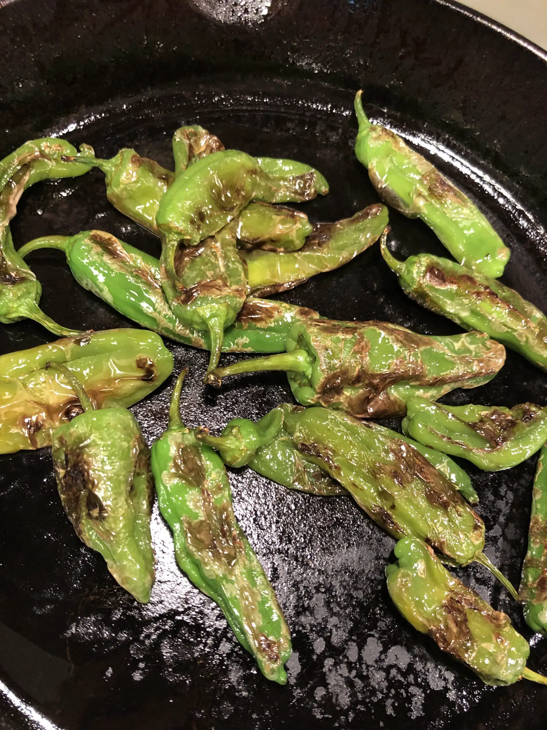 Blistered shishito peppers in a cast iron pan.