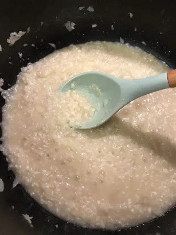 rice in broth in a pan with a blue silicone spoon