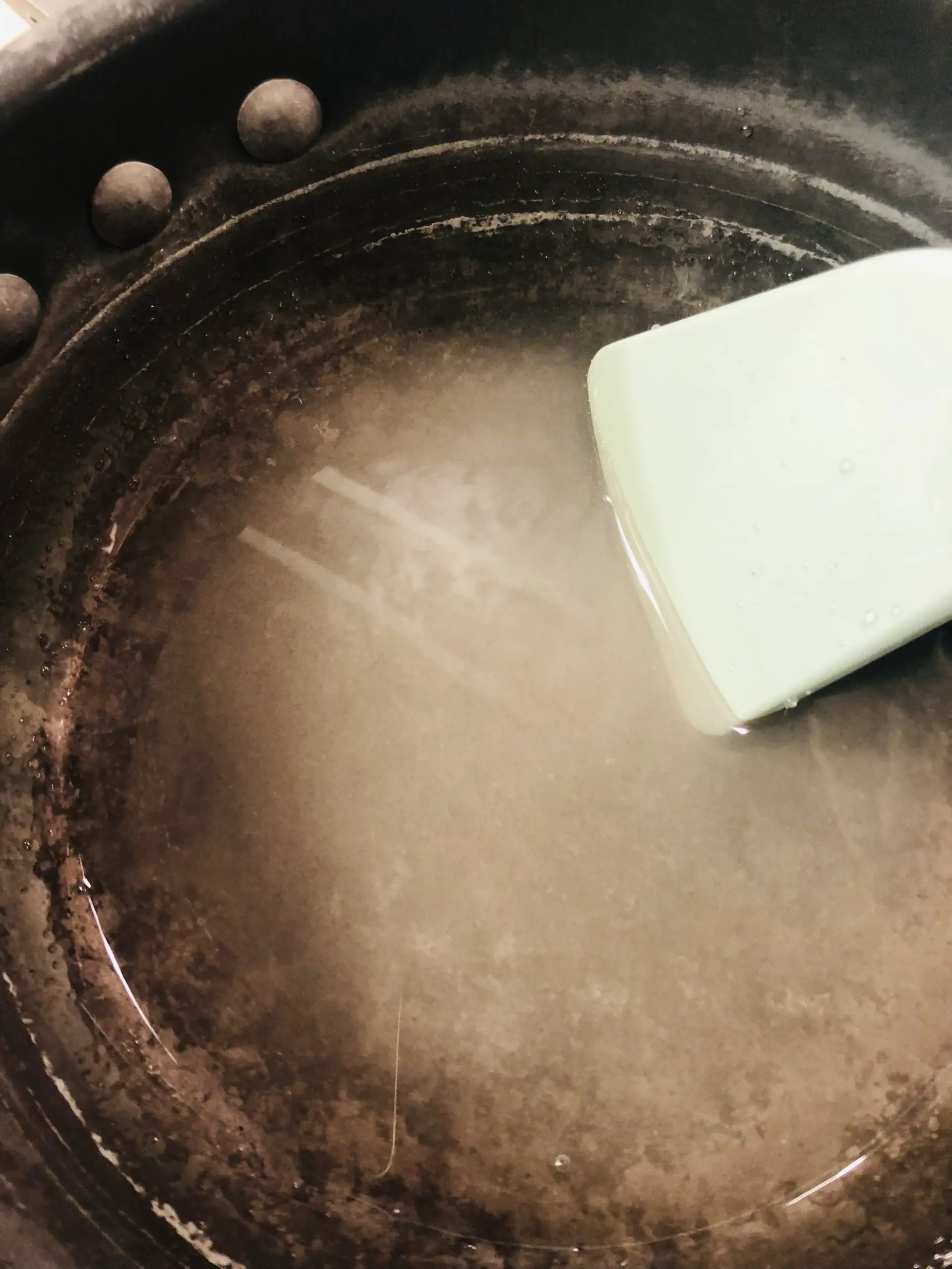 Sugar dissolved in vinegar in a saucepan with a blue utensil.