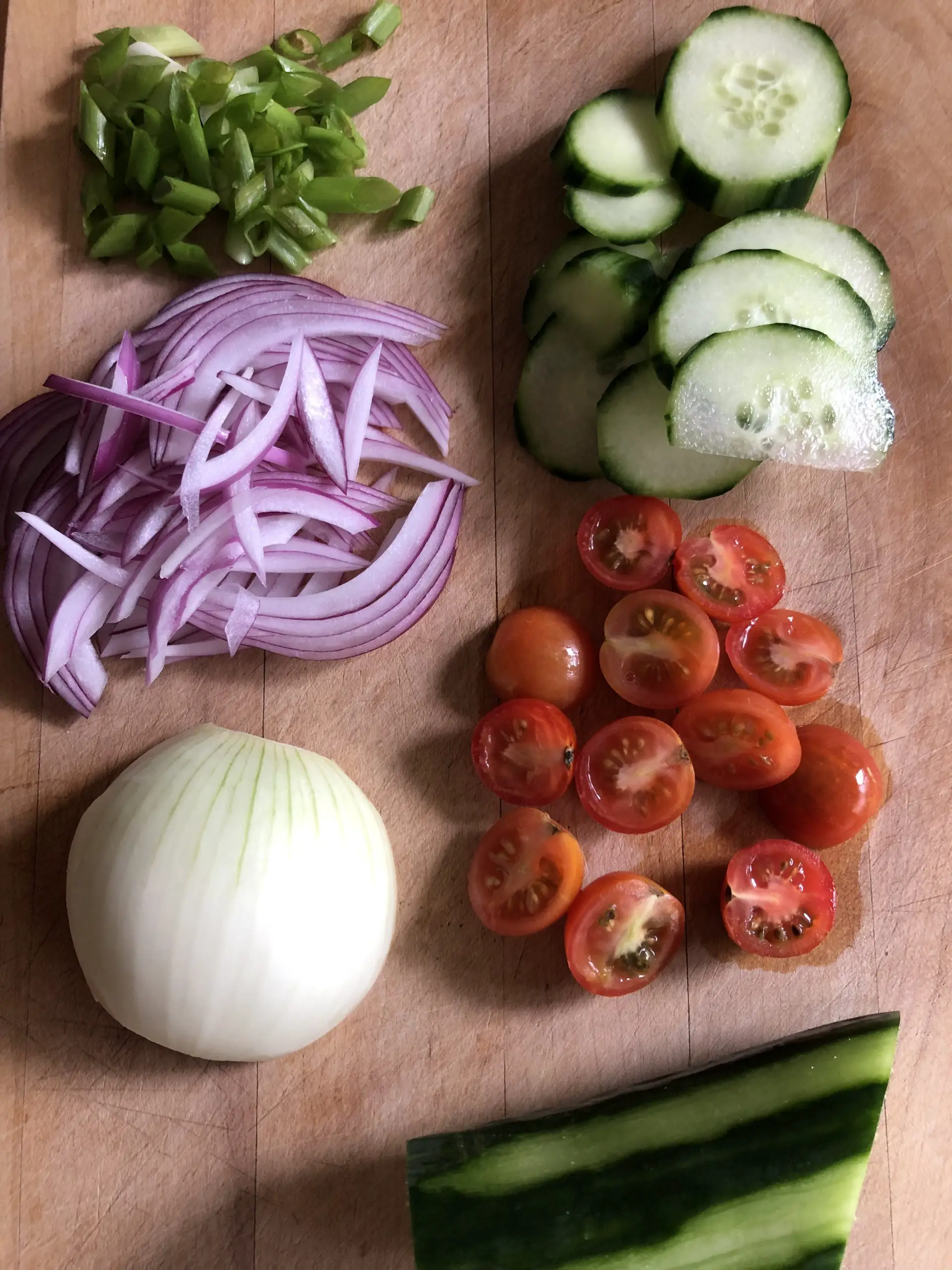 Sliced red onion, sliced green onion, half of a yellow onion, sliced cucumber, cherry tomatoes cut in half, cucumber with skin peeled off in intervals