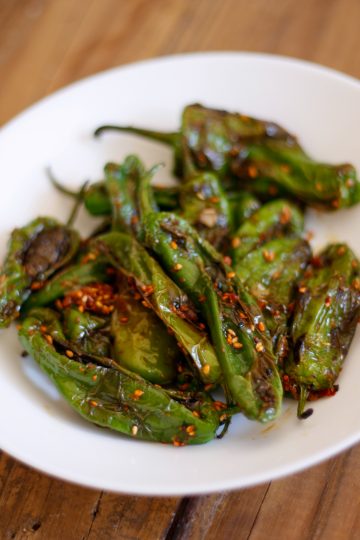 Blistered shishito peppers in a white bowl.