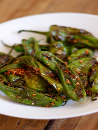 Blistered shishito peppers in a white bowl.