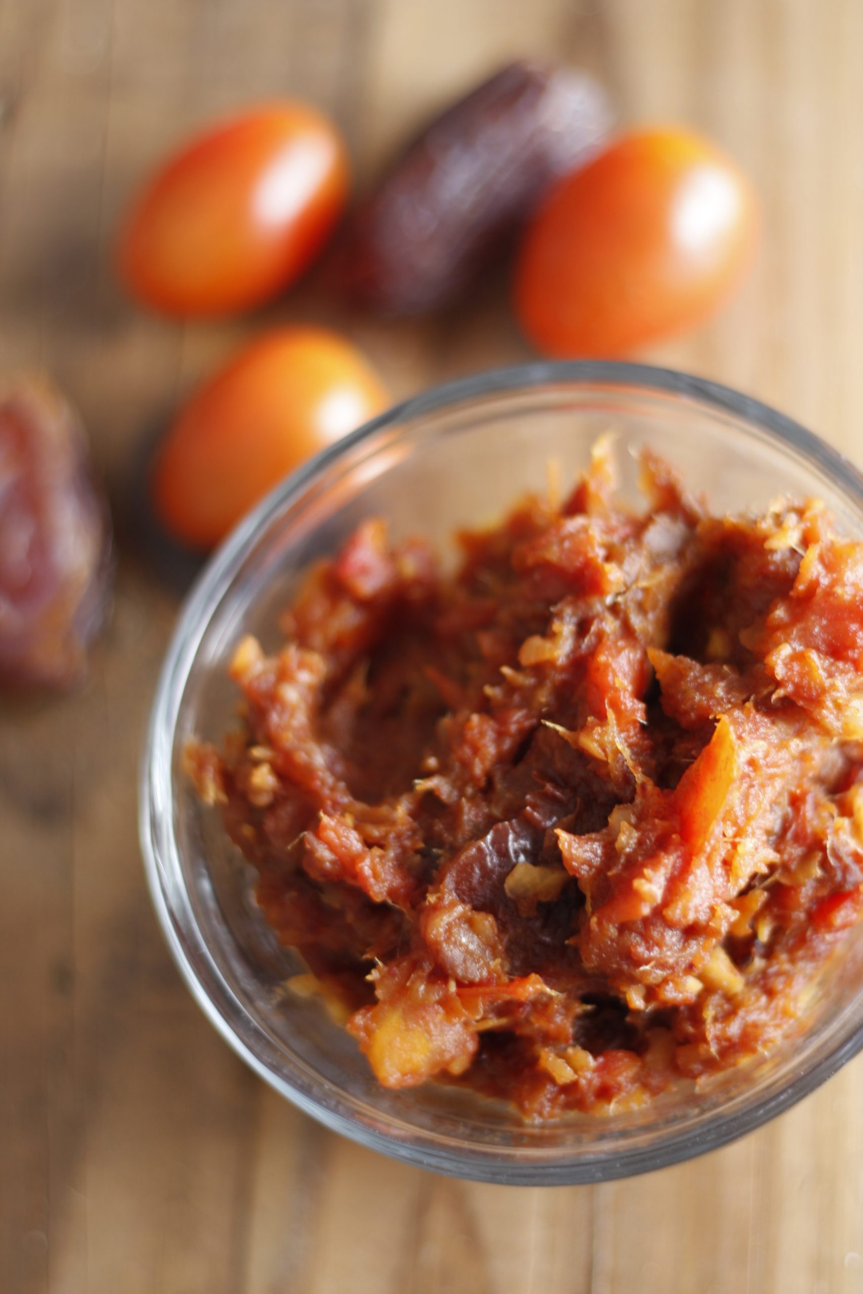 Tomato and date chutney in a glass bowl with tomatoes and dates in the background