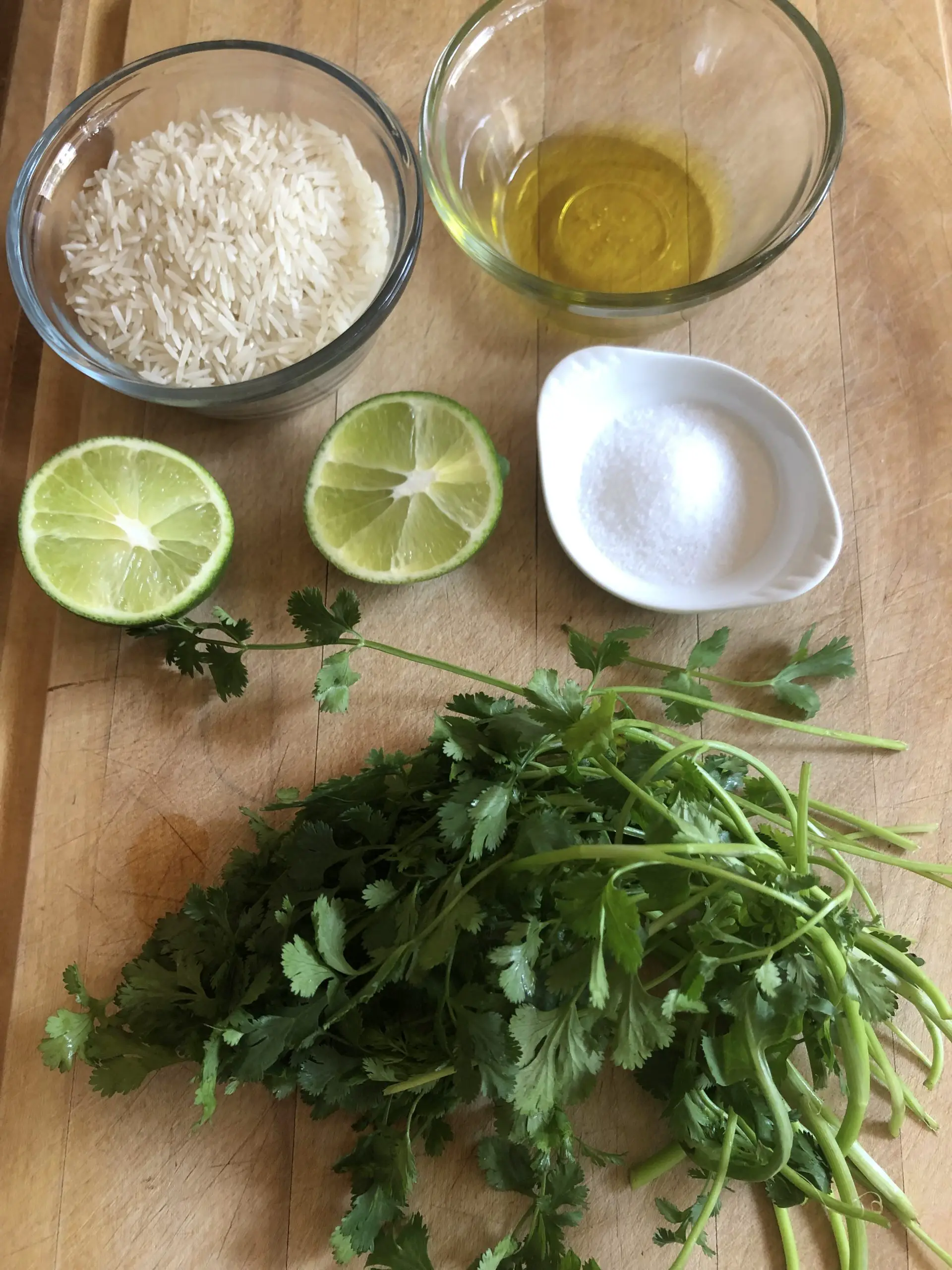 Bunch of cilantro, salt in a white dish, a cut up lime, rice in a glass bowl and olive oil in a glass bowl